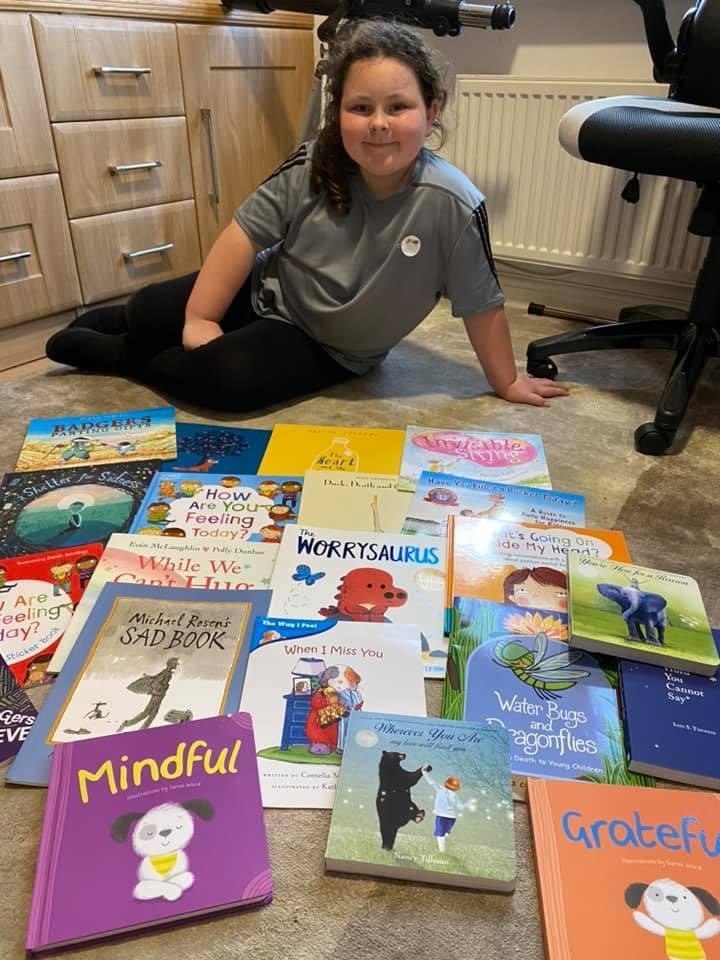 Young girl sat on floor in a home office with a selection of children's specialist bereavement books in front of her