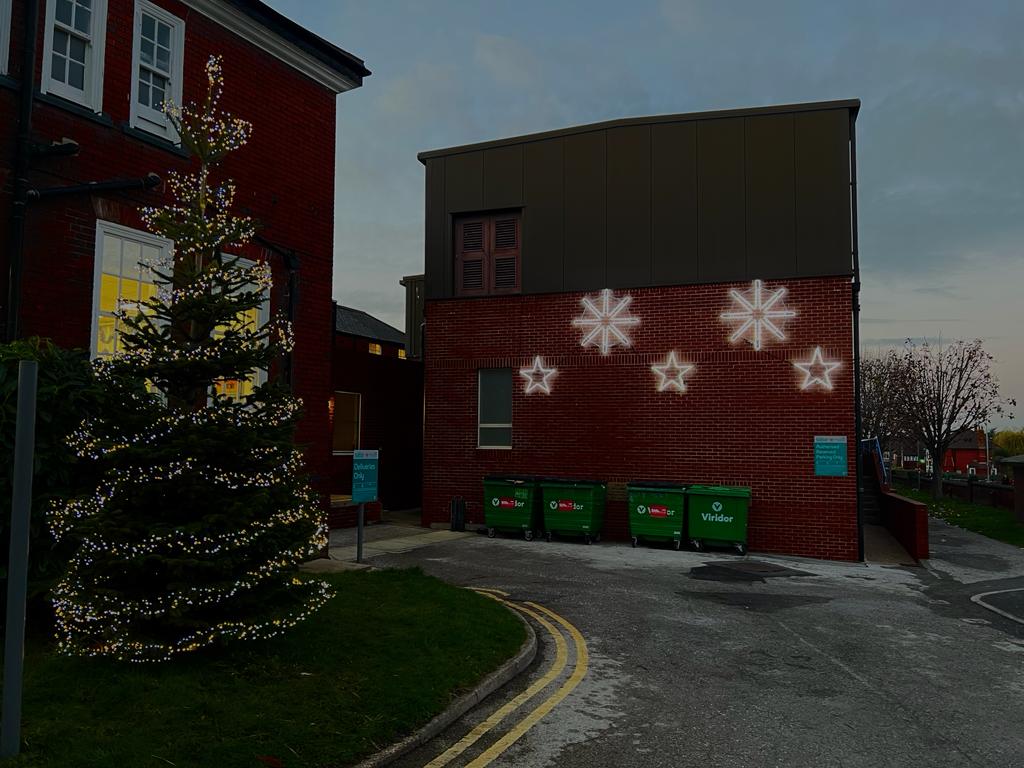 To the left we see a Christmas tree decorated in fairy lights, in the centre is a red brick building with 5 shining stars attached to the walls