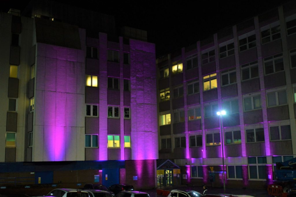 Image description: Image shows the exterior of the Women's and Children's Hospital at night, illuminated by multiple beams of purple light.