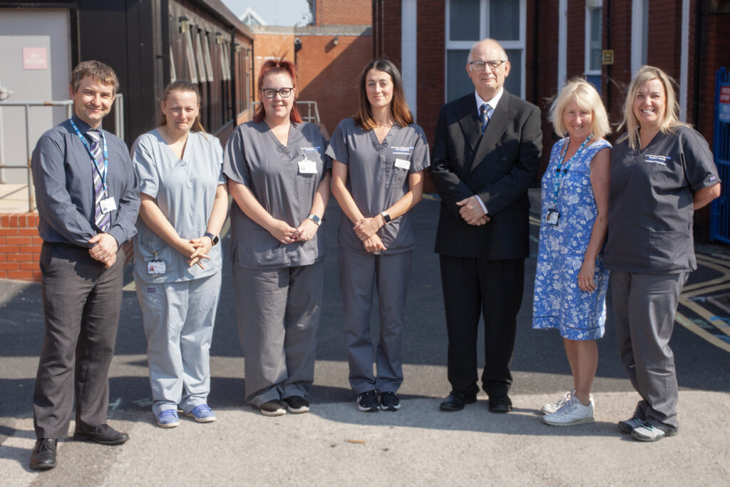 A photograph of all seven members of the AAA Screening Programme Team. They are stood outside in the sunshine in their clinical uniform and office wear. All are white, two are male and five are female staff members. 