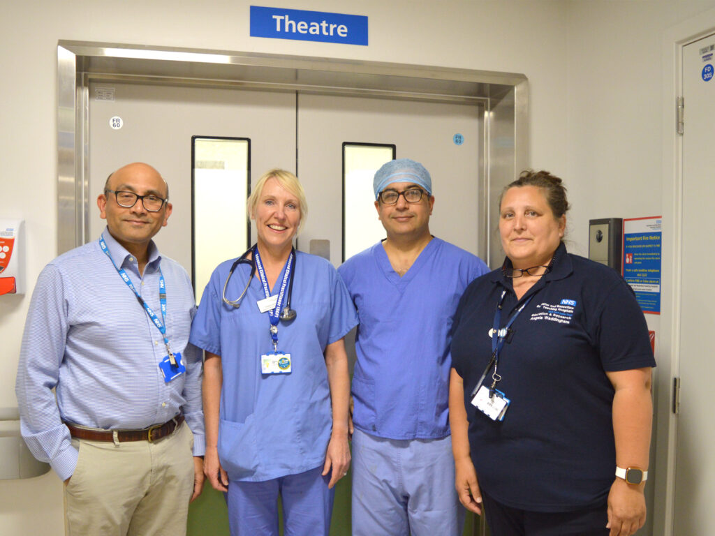 A photograph of Mr Arora and the FRUTI Study Team stood outside of the hospital's Theatres Department. Mr Arora and Mrs Bull are in blue scrubs., whilst Mr Vashista and Mrs Waddingham are in workplace attire. 