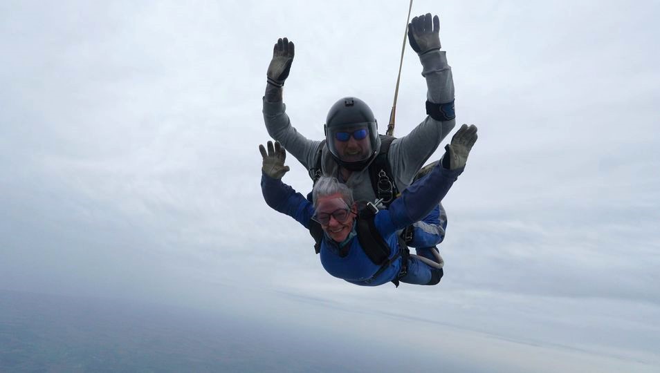 A staff member in a charity t-shirt is tandem skydiving