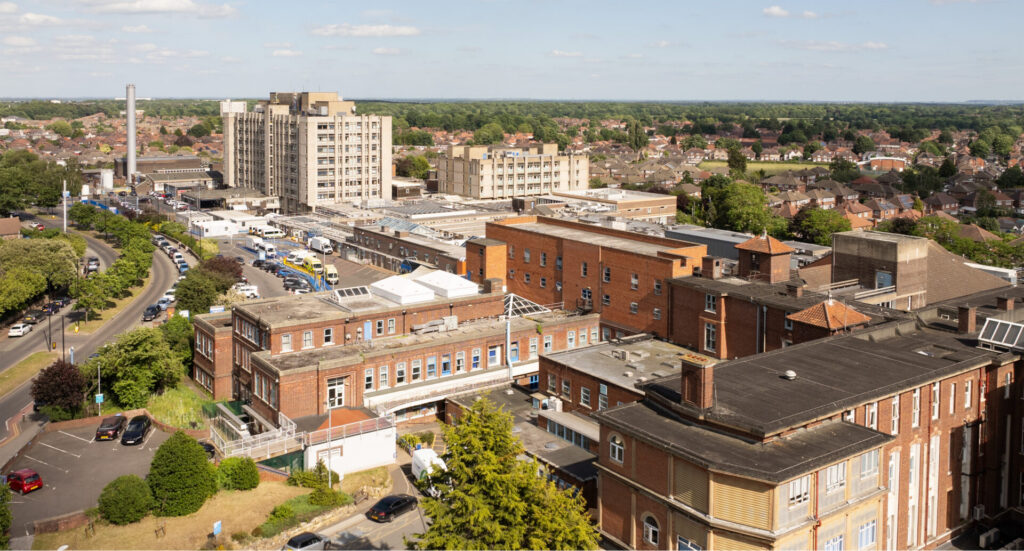 Drone view of the red brick west side of Doncaster Royal Infirmary on a sunny day, with the grey East Ward tower block in the background.